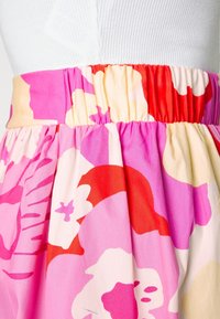 Hame floral dengan desain pink cerah, merah, dan krim. Pinggangnya dilengkapi dengan pita elastis, dan kainnya tampak ringan dengan lipatan.