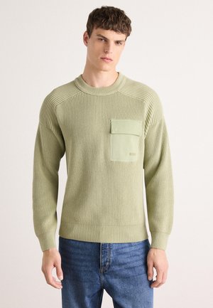 Light green ribbed knit sweater with a front pocket and crew neckline, paired with blue jeans. Smooth texture, casual design.