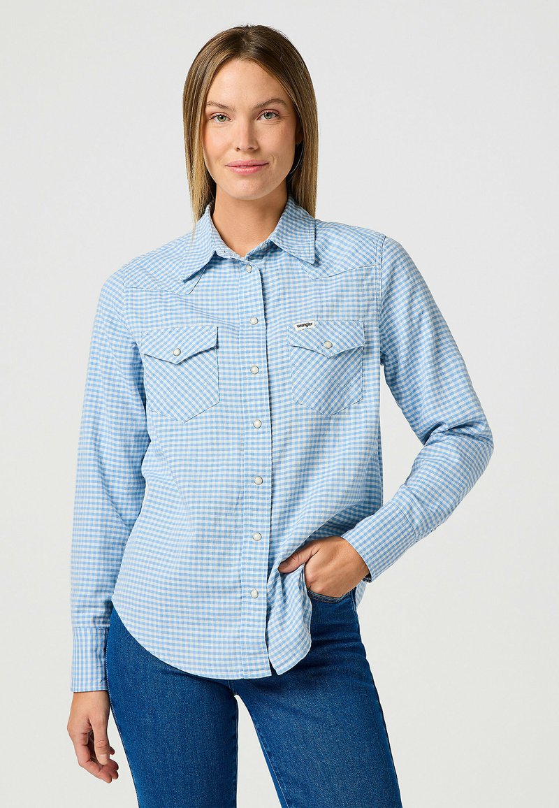 Jasnoniebieska koszula w krate z dwiema kieszeniami na piersi, kołnierzykiem zapinanym na guziki, długimi rękawami i srebrnymi guzikami. Materiał wydaje się miękki i gładki.