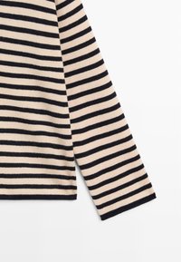 Beige långärmad stickad topp med marinblå horisontella ränder; har en rak skärning och ribbade muddar. Mjuk textur och lätt material.