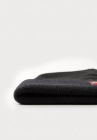 Beanie in maglia nera con risvolto, caratterizzato da un piccolo logo rosso e grigio. Texture morbida con un motivo a maglia stretta.