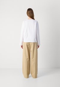 Haut à manches longues blanc et pantalon large beige. Tissu doux avec une coupe décontractée, présentant un design simple et des détails de couture minimalistes.
