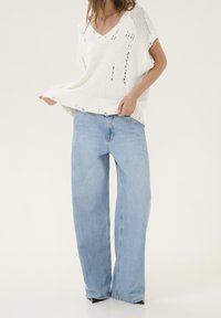 Top corto bianco a maglia con scollatura a V e dettagli strappati, abbinato a jeans larghi blu chiaro, dotati di vita alta e vestibilità dritta.