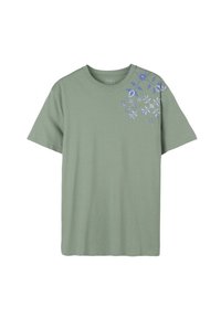 T-shirt vert à manches courtes en coton doux, avec des motifs floraux bleus sur l'épaule gauche et le haut de la poitrine.