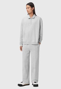 Helle graue Zip-Top-Jacke und passende Hose aus weichem Stoff. Die Jacke hat einen Kragen und einen lockeren Sitz; die Hose ist gerade geschnitten.