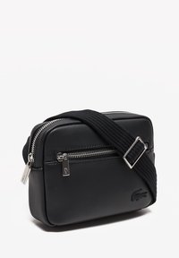 Melnā taisnstūra crossbody soma, izgatavota no teksturēta sintētiska materiāla, ar rāvējslēdzēja aizdari, regulējamu siksnu un smalku logo detaļu.