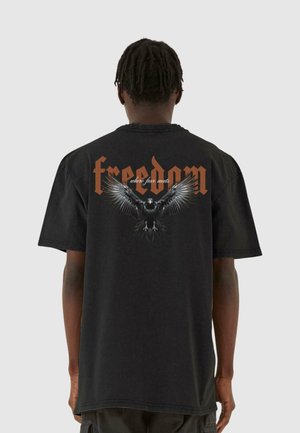 Sort bomuld t-shirt med en afslappet pasform. Har et grafik af en ørn og ordet "frihed" i orange, placeret på ryggen.