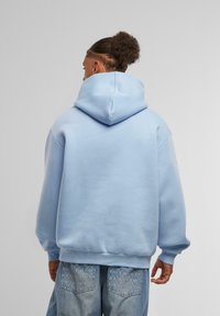 Lys blå oversized hettegenser med stor hette, ribbestrikkede mansjetter og nederkant. Myk stoff med en jevn tekstur, uten synlige logoer eller mønstre.