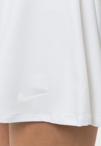 Valkoinen urheiluhame, joka on valmistettu sileästä ja teksturoidusta kankaasta, ja siinä on hillitty kohokuvioitu Nike-logo helman lähellä.