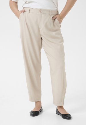 Beige trousers with a relaxed fit, pleats, and a button closure at the waist. Smooth fabric with a classic design, paired with black flats.