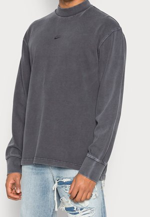 Graues Nike-Sweatshirt mit langen Ärmeln, hohem Kragen, weicher Textur und Logo auf der Vorderseite; kombiniert mit hellblauen Jeans im Used-Look.
