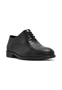 Chaussure en cuir noir à lacets avec une texture lisse, bout rond et un détail de couture sur le devant. Talon bloc bas.