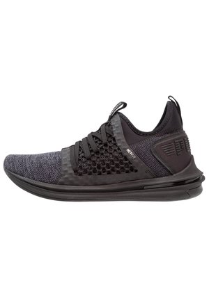 Baskets de sport noires avec tige en tricot, panneau latéral en mesh, languettes sur la languette et le talon, et semelle épaisse et rembourrée.