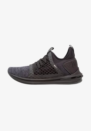 Baskets de sport noires avec tige en tricot, panneau latéral en mesh, languettes sur la languette et le talon, et semelle épaisse et rembourrée.