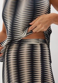 Completo top e gonna plissettati in bianco e nero, caratterizzati da un motivo a zigzag, vita elastica e una vestibilità comoda con dettagli a strati.