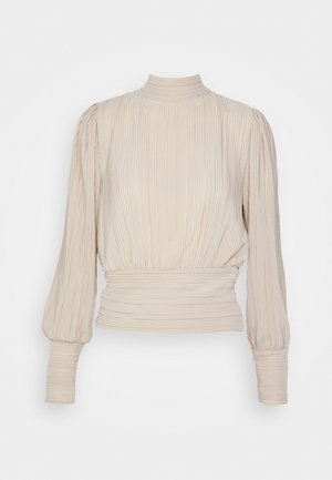 Blouse beige à manches longues avec col haut, texture plissée, manches bouffantes et large ceinture cintrée.