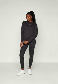 Completo felpa nera e leggings. La felpa ha un collo rotondo e un piccolo logo davanti; i leggings sono aderenti, con una superficie liscia e una lunghezza fino alla caviglia.
