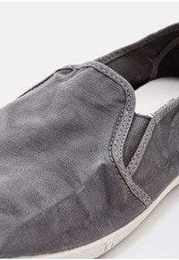 Sive slip-on čevlji iz teksturirane tkanine z vidno šivom, fleksibilno silhueto in meko notranjo oblogo. Bel podplat.