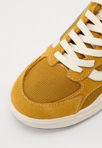 Gelbe Wildledersneaker mit Netzpaneelen, weißen Schnürsenkeln und gepolsterter Schuhkragen. Verfügt über eine Gummisohle und kontrastierende Nähakzente.
