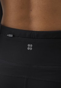 Sorte trenings leggings har en glatt, matt tekstur med en grå logo på midjen og et rent, enkelt design uten dekorasjoner.