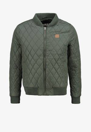 Vihreä tikkikuoritakki, jossa on joustava kaulus ja hihansuut. Takissa on edestä avattava vetoketju ja pieni logo-patch vasemmassa rinnassa.