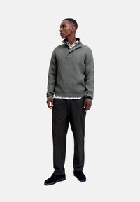 Green ribbed sweater with a half-zip collar, layered over a plaid shirt, paired with dark trousers and black shoes.