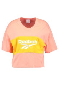 Zkrácený oversized tričko v světle růžové barvě se žlutým horizontálním panelem a bílým logem Reebok. Bavlněná tkanina s hladkým povrchem.