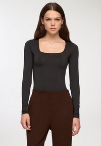 Czarny body z długim rękawem i kwadratowym dekoltem o gładkiej fakturze, połączone z brązowymi spodniami o wysokim stanie z bocznymi kieszeniami.