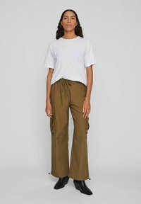 Tricou alb cu mâneci scurte, pantaloni cargo maro cu buzunare laterale, croială lejeră, material ușor, cizme negre până la gleznă, culori solide, design minimalist.