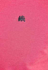 Różowa dziana tkanina z małym czarnym haftowanym logo, charakteryzująca się gładką fakturą i subtelnym, drobnym splotem.