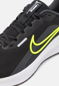 Sort mesh sneakers med gul accent logo, hvid mellemsål, teksturerede detaljer på overdelen og flade snørebånd. Har et støttende design.