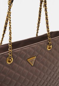 Brun quiltet tote taske med guldhardware, der har en kædestrop og en trekantet logo-plade. Glat tekstur og åbent topdesign.