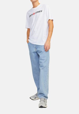 Weißes T-Shirt mit kurzen Ärmeln und "JACK & JONES"-Logo, kombiniert mit hellblauen gerade geschnittenen Jeans und grauen Sneakers mit schwarzen Akzenten.