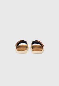 Sandales marron avec une semelle beige, dotées d'un design ouvert, d'une doublure intérieure bleue et de sangles ajustables. Construction plate et minimaliste.