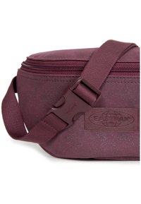 Punainen, teksturoitu kangaskassi vetoketjulla. Säädettävä olkahihna ja muovinen solki. Sivussa näkyvä logopatch.