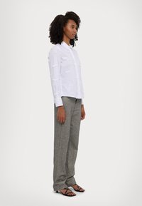 White shirt with bow details, paired with gray patterned trousers and black heeled sandals. The shirt features a button-down front and long sleeves.