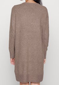 Abito lavorato a maglia marrone con maniche lunghe, scollatura rotonda e vestibilità ampia. La texture è morbida e leggermente spessa, con orlo a coste.