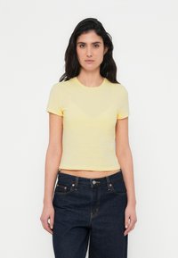 Keltainen lyhythihainen T-paita, valmistettu pehmeästä puuvillasta, lyhennetty malli, sileä pinta, pyöreä kaula-aukko ja minimaaliset saumat.