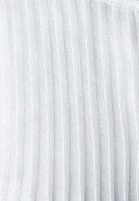 Tessuto bianco con pieghe verticali, superficie liscia, finitura morbida e leggera lucentezza, ideale per abbigliamento o applicazioni interne.