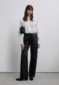 Witte blouse met knopen, voorzien van een geplooide kraag en lange mouwen, gecombineerd met een zwarte leren broek met hoge taille. Zwarte handtas en enkellaarsjes.