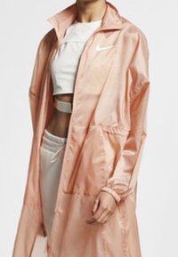 Rosa nylon vindjacka med hög krage, framfickor och elastiska muddar. Kombination med en vit topp och träningsbyxor.