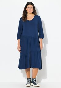 Abito blu navy, di lunghezza al ginocchio, con scollatura a V e maniche a tre quarti. Presenta balze a strati sul fondo e un tessuto morbido e texturizzato.