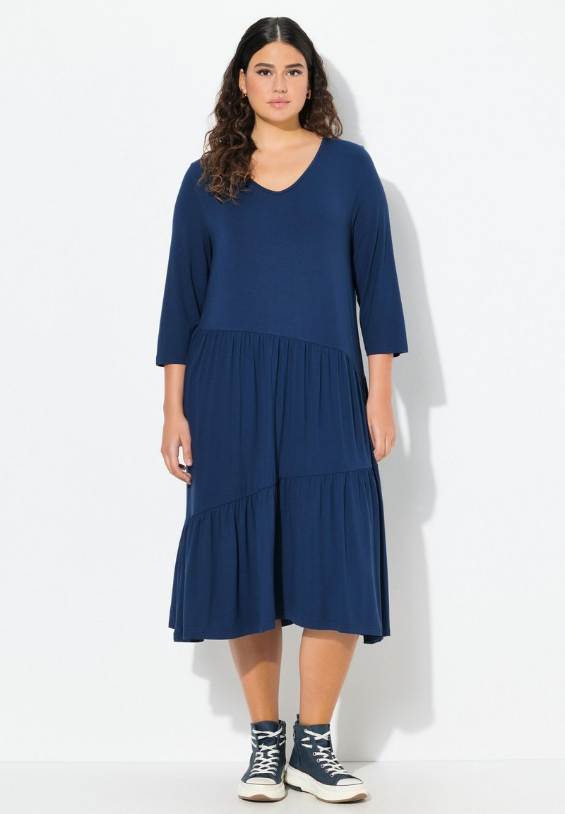 Abito blu navy, di lunghezza al ginocchio, con scollatura a V e maniche a tre quarti. Presenta balze a strati sul fondo e un tessuto morbido e texturizzato.