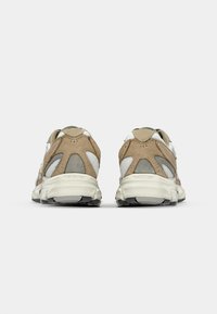 Beige og grå trening-sko med en teksturert semsket skinn- og mesh-overdel, med polstret krage, tykk såle og gummisåle med mønster.