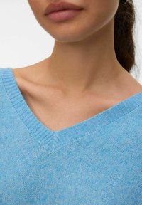 Pull bleu clair à col en V en tissu tricoté doux, avec des détails côtelés le long de l'encolure et des épaules.