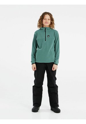 Pullover in pile verde con colletto a mezza zip, motivo texture, dettaglio logo nero, abbinato a pantaloni impermeabili neri e stivali.