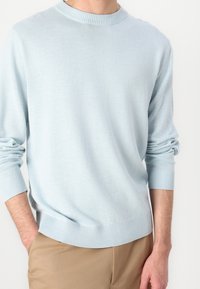 Ljusblå stickad tröja med rund halsringning och ribbade muddar och fåll. Mjuk textur, klassisk passform. Matchas med tanfärgade byxor.