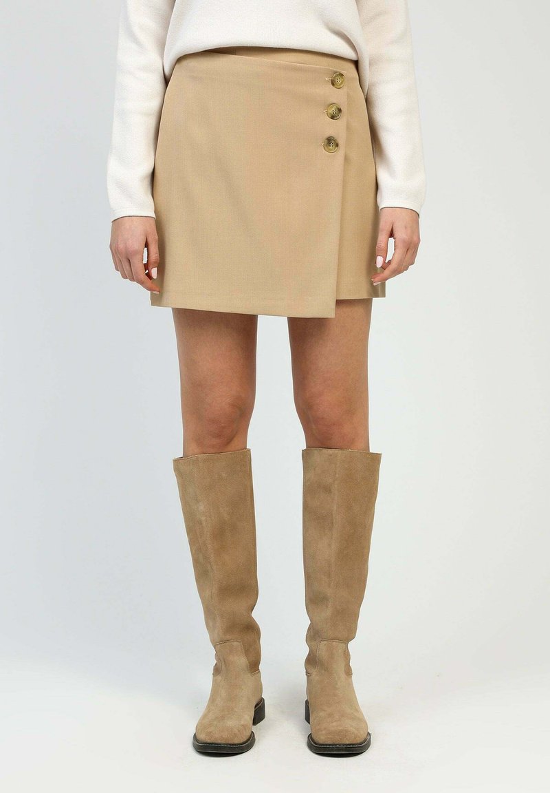 Jupe portefeuille beige en tissu lisse, ornée de trois boutons dorés à l'avant et au design épuré et minimaliste.