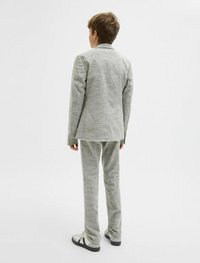 Ljusgrå, texturerad kostym med en enfärgad kavaj och rakbenade byxor, kombinerad med vita sneakers och svarta accenter.