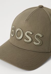 Casquette de baseball kaki avec broderie "BOSS" en vert olive clair. Caractérisée par une forme structurée et un tissu texturé avec des coutures contrastantes.